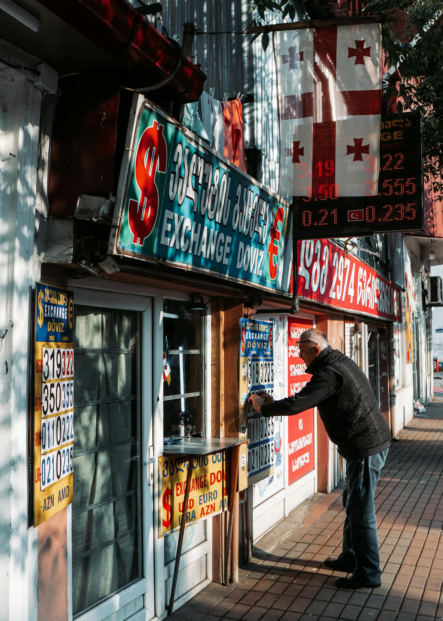 Man at currency exchange booth on a Batumi sidewalk, showcasing exchange rates.